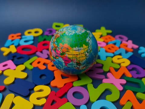 Small terrestrial globe ball centered on a bed of colorful wooden letters and numbers against a blue background