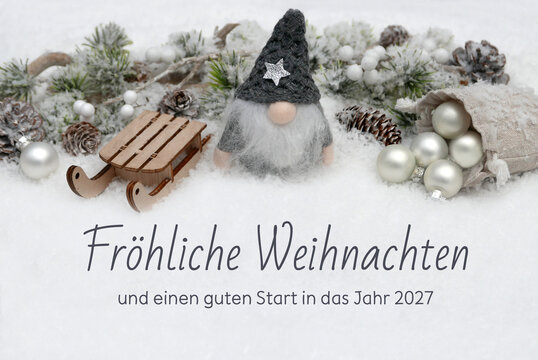 Weihnachtskarte:  Winterliche Kulisse mit Wichtel, Weihnachtskugeln und Schlitten im Schnee der Text Fr&ouml;hliche Weihnachten und einen guten Start in das Jahr 2027 ist in den Schnee geschrieben.