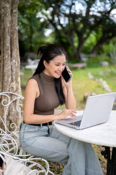 Happy Asian Freelancer Calling On Phone While Working On Laptop