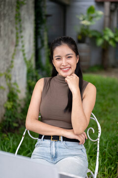 Smiling Asian Woman Sitting On White Chair In Backyard