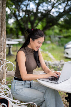 Joyful Asian Woman Typing On Laptop In Outdoor Green Garden