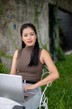 Asian Businesswoman Working On Laptop In Outdoor Garden Cafe