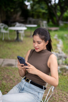 Focused Asian Woman Browsing Smartphone At Outdoor Cafe Table