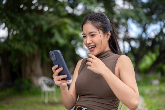 Excited Asian Woman Looking At Smartphone In Garden Outdoors