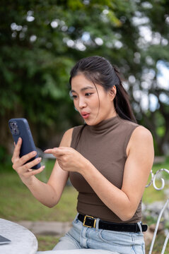 Surprised Asian Woman Pointing Finger At Smartphone Screen Outdoors