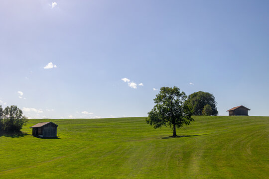 Bavarian countryside landscape, A traditional wooden barns standing alone on a rolling hill, Lush green grass meadow against majestic Alpine mountains under blue sky and white clouds, Bavaria, Germany