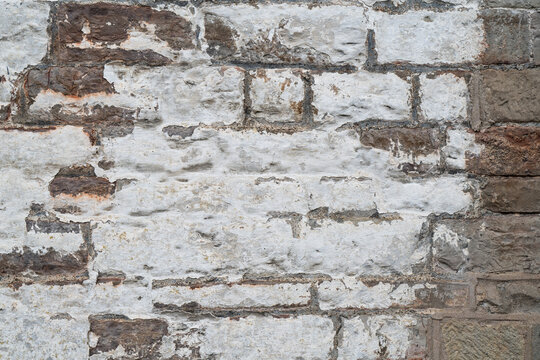 Old whitewashed brick wall texture background with exposed brown bricks and heavily worn patchy finish