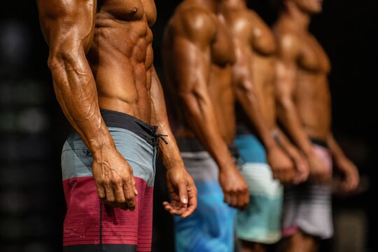 Muscular male bodybuilders standing in lineup on stage during physique competition