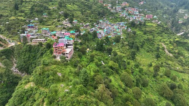 Drone shot of colorful traditional guest houses in Tosh village perched on a steep Himalayan slope in Parvati Valley, India.