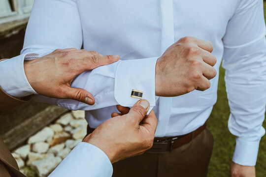 Man adjusting elegant gold cufflink on white shirt before formal event