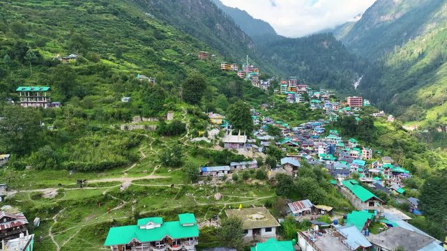 Lateral aerial tracking shot of colorful traditional guest houses in Tosh village perched on a steep Himalayan slope in kheerganga valley, Himachal, India.