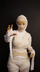 Fototapeta na wymiar woman wrapped in bandages as mummy costume for halloween with grabbing hand