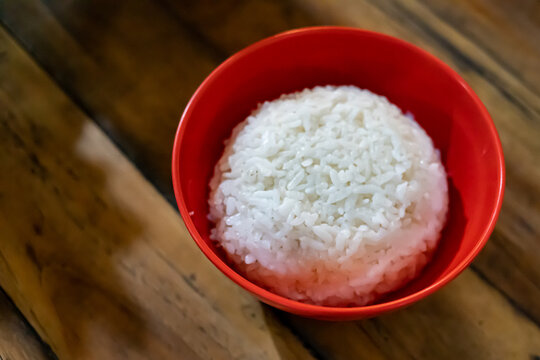 Freshly cooked steamed white rice neatly served in a bright red bowl placed on a rustic wooden surface, perfect for Asian cuisine and healthy staple food visual concepts.