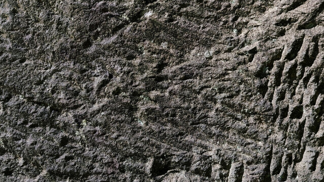 Dark grey rough chiseled rock stone wall surface texture background with grooves