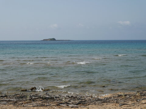 Peaceful coastal landscape with turquoise ocean water, a small rocky island on the horizon viewed from the beach