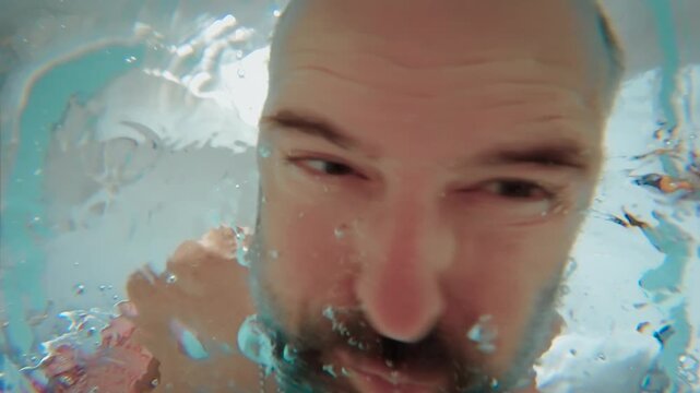 Distressed man screaming underwater and shaking head from side to side, view from bottom of bathtub. Depression and panic attack with intense emotional breakdown. Mental health crisis, anxiety and