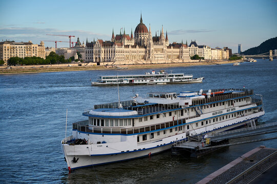 Grand Jules Boat Hotel and cruise ships docked along the Danube River with the Hungarian Parliament Building in Budapest, Hungary