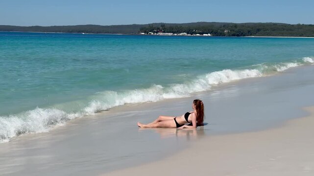 A girl in a bikini lies on the white sand of the famous Hyams Beach, gently washed by soft waves, near Wollongong, a paradise holiday destination, Jervis Bay, New South Wales, Australia.