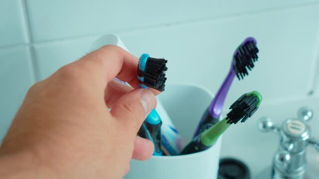 Hand taking blue toothbrush from holder with colorful dental care supplies. Morning oral hygiene routine at bathroom sink. Personal dental health and everyday tooth brushing preparation concept