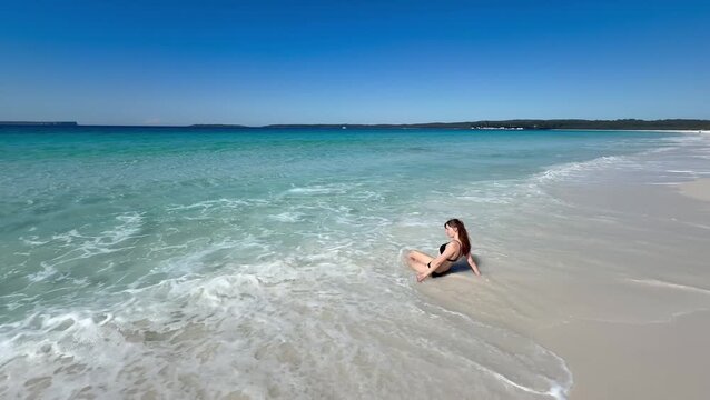 A girl in a bikini lies on the white sand of the famous Hyams Beach, gently washed by soft waves, near Wollongong, a paradise holiday destination, Jervis Bay, New South Wales, Australia.