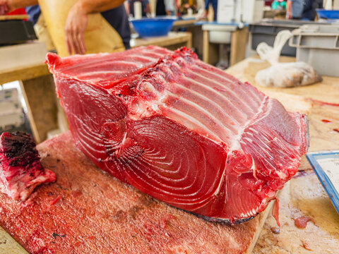 A professional fishmonger cutting a huge raw red fresh tuna fish on a wooden counter at a fish market, Funchal, Madeira, Portugal.
