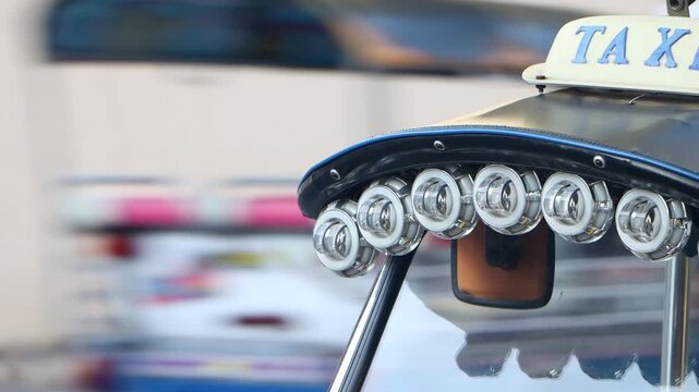 Close-up detail of a row of customized LED headlights and a taxi sign on the roof of a traditional Tuk Tuk in Bangkok