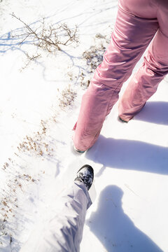 First-person perspective of hikers wearing insulated pants and winter footwear while walking along a snow-covered trail in sunny weather. Winter trekking, recreation and mountain adventure concept.