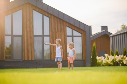 Young children running barefoot and playing together on green lawn near a modern house in warm evening sunlight. Active childhood, outdoor play, summer leisure and carefree lifestyle concept.