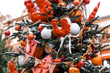Winter Christmas tree with orange decorations, gifts, and a cockerel on a stick. Beautiful Christmas background. Concept for the New Year 2027.  © Юлия Клюева