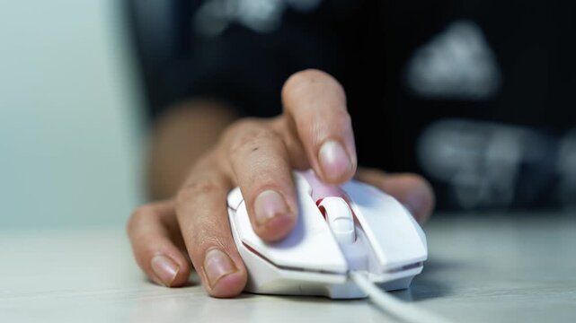 Hand Using a Wired Computer Mouse, Close-up of a hand using a white wired computer mouse on a desk, showing everyday technology use, work, gaming, and online activity.