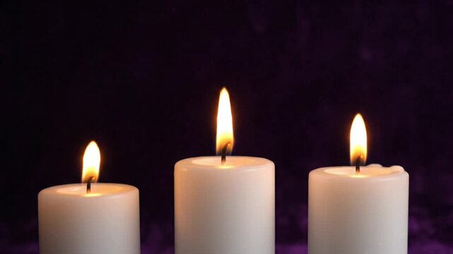 Three warm glowing white candles burning brightly against a dark purple background, symbolizing peace, hope, and remembrance.