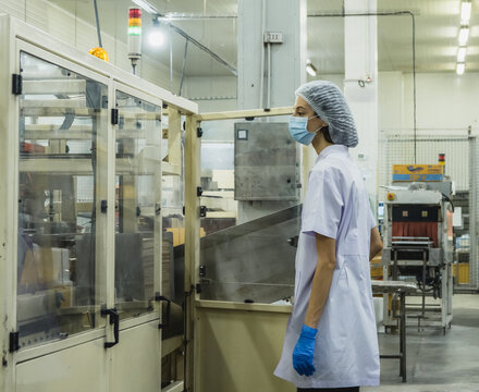 Female Factory Operator Inspecting Packaging Machine Food Process Plant Female technician protective hygienic coat hairnet mask operating industrial packaging machinery quality assurance concept.