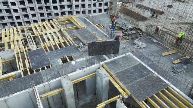 Aerial oblique view of construction crew lifting and aligning formwork panels on reinforced concrete slab during building site construction worksite operations