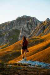 Obraz premium Young woman standing on a mountain peak at sunset, arms open or enjoying the view, embracing nature and freedom in the mountains in Durmitor National Park, Montenegro.