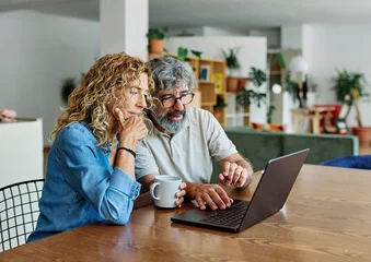 Fotobehang Onderzeeër Portrait of a lovely senior mature couple using a laptop together and having fun drinking coffee or tea sitting at a table at home  © Lumos sp