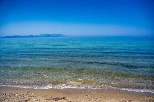 View of clear blue sea and distant island from sandy beach.