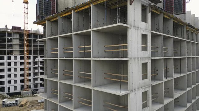 Unfinished multistory concrete building corner with repeating room openings grid, temporary timber guardrails, exposed slabs, and overcast sky during residential construction