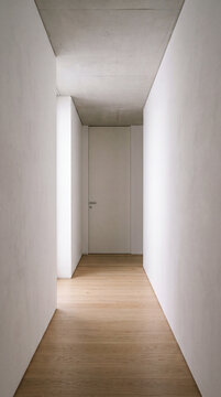 Minimalist hallway with warm wooden floor leading toward soft natural light