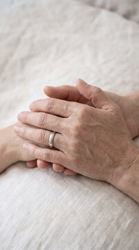 Close-up of clasped hands resting gently on soft linen bedding at home