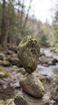 Stacked stones balanced on mossy rocks beside a flowing forest mountain stream