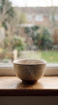 Steaming ceramic bowl resting on a windowsill overlooking a soft garden view
