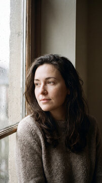 Woman gazing thoughtfully out a window bathed in warm indoor afternoon light