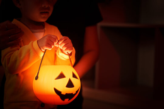 Child holding glowing Halloween pumpkin bucket lantern at home