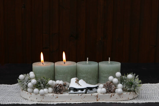 Modern Advent arrangement for the second Sunday of Advent featuring four sage-green candles and small white ice skates against a dark wood background, with space for text.