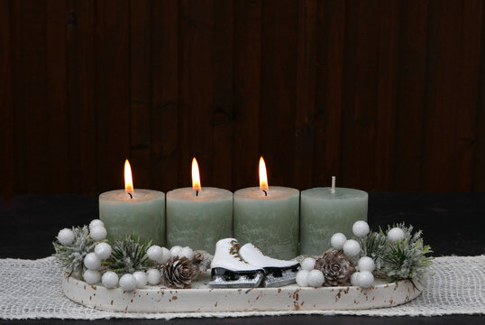 Modern Advent arrangement for the third Sunday of Advent featuring four sage-green candles and small white ice skates against a dark wood background, with space for text.