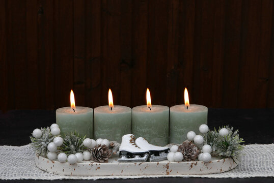 Modern Advent arrangement for the fourth Sunday of Advent featuring four sage-green candles and small white ice skates against a dark wood background, with space for text.