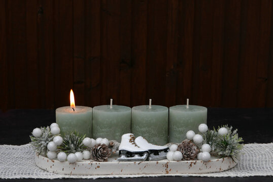 Modern Advent arrangement for the first Sunday of Advent featuring four sage-green candles and small white ice skates against a dark wood background, with space for text.