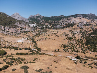 Aerial view of a dry golden valley with scattered olive groves and white buildings nestled among rugged rocky mountains under a clear blue sky in Grazalema, Spain © Felix Morion