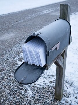 Vintage metal mailbox stuffed with white envelopes. Rural mail delivery on a winter day. Full mailbox with letters and correspondence.