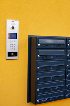 Modern intercom system with security camera and numerical keypad next to apartment mailboxes on a bright yellow wall close up view.